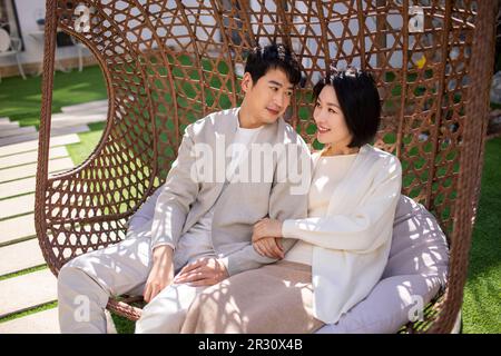 Glückliches, junges chinesisches Paar, das sich auf einem Hängestuhl entspannt Stockfoto