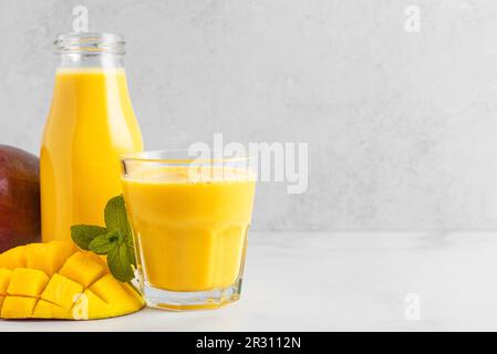 Mango-Smoothie in Flasche und Glas mit frischem Obst. Tropisches Sommergetränk auf weißem Hintergrund Stockfoto