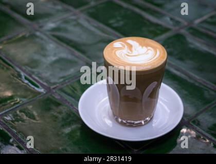 Flacher weißer Kaffee in einer Tasse aus Glas auf einem grün gefliesten Tisch. Speicherplatz kopieren. Stockfoto