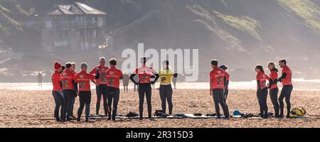 Ein Panoramabild einer Gruppe von Bodyboardern, die einem Lehrer während einer Bodyboardstunde am Fistral Beach in Newquay in Cornwall im zuhören Stockfoto