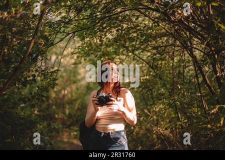 Weibliche Reisende mit Kamera, die wegschaut, während sie im Wald steht Stockfoto