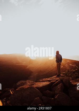 Ein Mann, der auf einem Berg steht und den Sonnenaufgang beobachtet Stockfoto