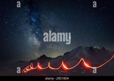 Milchstraße über dem Mt Rainier mit Taschenlampen am Pfad Stockfoto