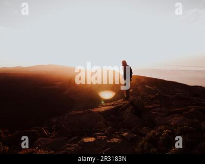Ein Mann steht auf dem Gipfel des Berges und sieht den Sonnenaufgang Stockfoto