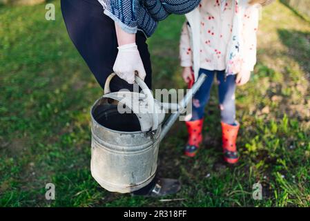 Großmutter mit ihrer Enkelin, die eine Gießkanne im Freien hält. Stockfoto