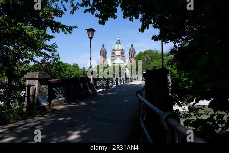 München, Deutschland. 22. Mai 2023. Ein Mann steht in der Sonne auf der Seilbahn auf der Isar. Die Kirche von St. Luke ist im Hintergrund zu sehen. Kredit: Sven Hoppe//dpa/Alamy Live News Stockfoto