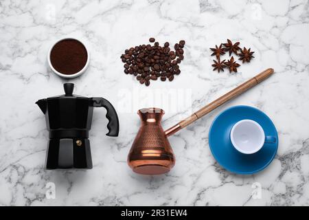 Flache Bettwäsche mit Geysirkaffeemaschine und gerösteten Bohnen auf weißem Marmortisch Stockfoto