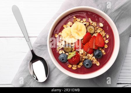 Köstliche Smoothie-Schüssel mit frischen Beeren, Banane und Müsli auf weißem Holztisch, flach liegend Stockfoto