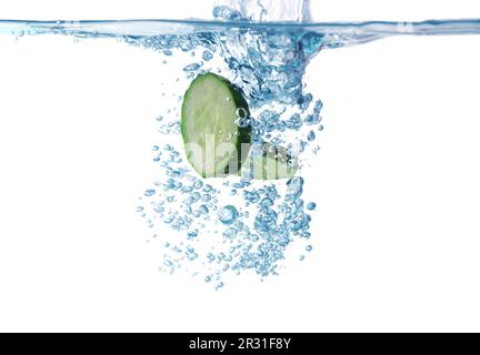 Frische Gurkenscheiben, die auf weißem Hintergrund ins Wasser fallen, Nahaufnahme Stockfoto
