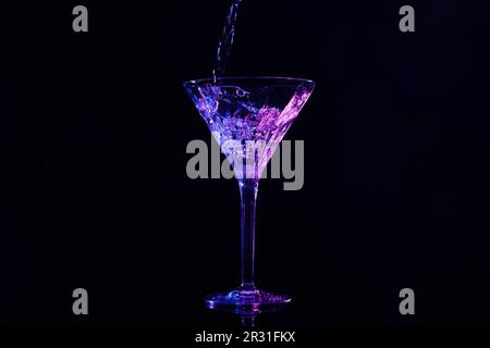 martini in Glas gießen, in Neonlichtern auf dunklem Hintergrund Stockfoto