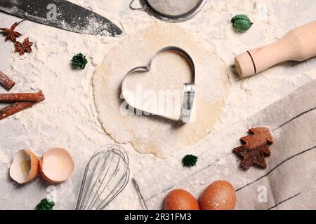 Flach liegend mit herzförmigem Keksschneider, Teig und Zutaten auf dem Tisch Stockfoto