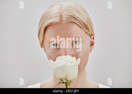 Minimalporträt eines hübschen jungen Mädchens mit Albinismus, das weiße Rose hält Stockfoto