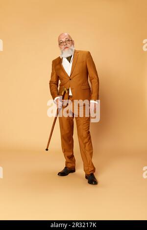 Porträt eines bärtigen, reifen, kahlen Mannes in elegantem, klassischem Anzug und wandelnder Pose mit ernstem Ausdruck vor Studiohintergrund Stockfoto