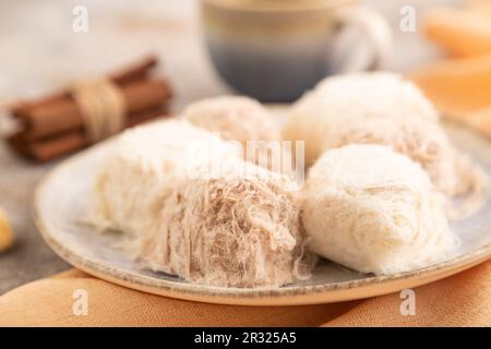 Traditionelle arabische Süßigkeiten pishmanie und eine Tasse Kaffee auf braunem Betonhintergrund und orangefarbenem Leinentuch. Seitenansicht, Nahaufnahme, selektiver Fokus. Stockfoto