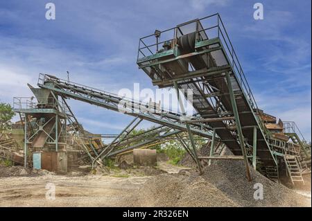 Brechmaschinen, Konusbrecher, Förderer von Granitkiesstein in einem Steinbruch im Tagebau. Minningindustrie Kies Steinbruch Transport Stockfoto