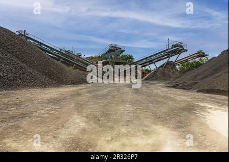 Brechmaschinen, Konusbrecher, Förderer von Granitkiesstein in einem Steinbruch im Tagebau. Minningindustrie Kies Steinbruch Transport Stockfoto