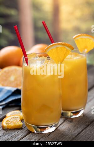 Orangensaftcocktail mit Orangenscheiben und frischen Orangen auf einem alten Holztisch mit Naturkulisse Stockfoto