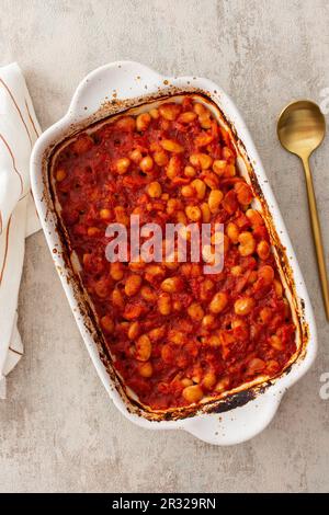 Gesundes Frühstück und Mittagessen, gedünstete weiße Bohnen mit Karotten, Zwiebeln und Tomaten, Blick von oben auf eine ovale Keramikrösterei mit gedünsteten Hülsenfrüchten Stockfoto