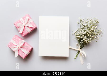 Hochzeitsmodell mit weißer Papierliste und Blumen Zigeuner auf farbigen Tisch Blick flach liegend. Leere Grußkarten und Briefumschläge. Wunderschönes Blumendesign Stockfoto