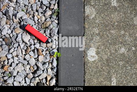 Ein weggeworfenes rotes Vapé, das auf Kies neben Betonpflaster weggeworfen wurde. Stockfoto