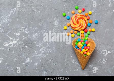 Waffelkonus voller traditioneller Süßigkeiten, die auf farbigen Hintergrund fallen, mit Platz für Kopien. Frohes Weihnachtsangebot. Stockfoto