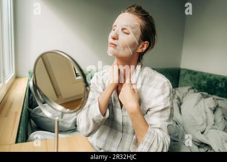 Eine Frau benutzt eine feuchtigkeitsspendende Maske für ihre häusliche Pflege. Selbstpflegekonzept. Stockfoto