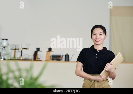 Porträt einer lächelnden jungen Kellnerin im Café, die ein gewohntes Brett zum Sushi-Servieren hielt Stockfoto