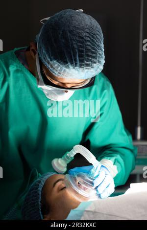 Vielfältiger männlicher Chirurg, der der Patientin eine Sauerstoffmaske während der Operation im Operationssaal gibt Stockfoto