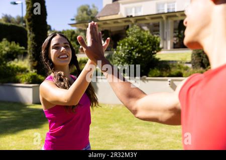 Glückliches, vielseitiges Paar, das Yoga-High-Fiving und ein Lächeln im sonnigen Garten übt Stockfoto