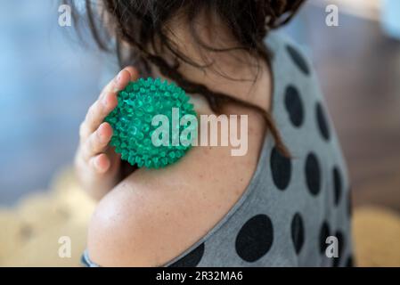 Frau mit grünem, stacheligem Massageball auf der Schulter für Muskelentspannung und Schmerzlinderung, Selbstmassagetherapiewerkzeug für myofasziale Lockerung und Spannung t Stockfoto