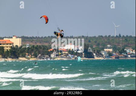 Ein Kitesurfer springt hoch in die Luft, und beide Füße lösen sich vom Brett am Strand in Mui Ne, Vietnam. Stockfoto