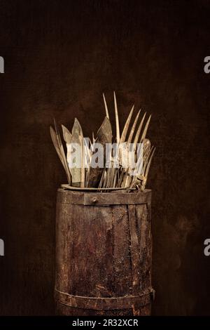Antiker Holzfass mit Gabeln, Messern und Löffeln vor einem verwitterten braunen Hintergrund Stockfoto