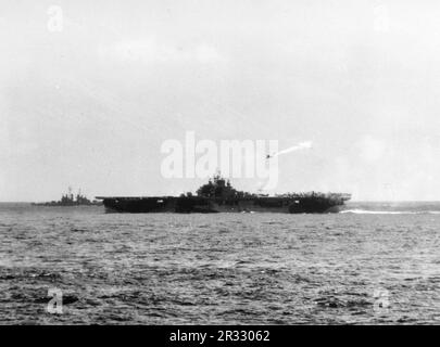 Ein bemerkenswertes Foto, auf dem die USS Essex am 25. November 1944 von einem Kamikaze östlich von Luzon, Philippinen, getroffen wird. Als Japan Ende 1944 mit einer Niederlage konfrontiert war, entschied es sich, US-Schiffe mit Selbstmordattentaten, bekannt als Kamikaze, zu zerstören. Diese Angriffe waren eine starke physische und psychologische Waffe und versenkten insgesamt 47 Schiffe zu einem Preis von mehr als 3000 Piloten und Flugzeugen. Ende 1944 war die US-Marine so groß, dass die Verluste unbedeutend waren und den Verlauf des Krieges nicht veränderten. Stockfoto