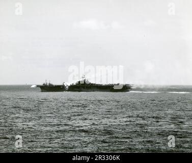 Ein bemerkenswertes Foto, das zeigt, wie die USS Essex von einem Kamikaze östlich von Luzon, Philippinen, getroffen wird, 25. November 1944. Die Rauchspur aus dem Flugzeug ist noch immer in der Luft sichtbar, was zum Aufprall und zur Explosion führt. Als Japan Ende 1944 mit einer Niederlage konfrontiert war, entschied es sich, US-Schiffe mit Selbstmordattentaten, bekannt als Kamikaze, zu zerstören. Diese Angriffe waren eine starke physische und psychologische Waffe und versenkten insgesamt 47 Schiffe zu einem Preis von mehr als 3000 Piloten und Flugzeugen. Ende 1944 war die US-Marine so groß, dass die Verluste unbedeutend waren und den Verlauf des Krieges nicht veränderten. Stockfoto