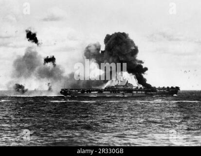 Die USA Der Flugzeugträger USS Intrepid (CV-11) der Marine brannte, nachdem das Schiff von zwei japanischen Kamikaze-Flugzeugen getroffen wurde, am 16. April 1945. Als Japan Ende 1944 mit einer Niederlage konfrontiert war, entschied es sich, US-Schiffe mit Selbstmordattentaten, bekannt als Kamikaze, zu zerstören. Diese Angriffe waren eine starke physische und psychologische Waffe und versenkten insgesamt 47 Schiffe zu einem Preis von mehr als 3000 Piloten und Flugzeugen. Ende 1944 war die US-Marine so groß, dass die Verluste unbedeutend waren und den Verlauf des Krieges nicht veränderten. Stockfoto