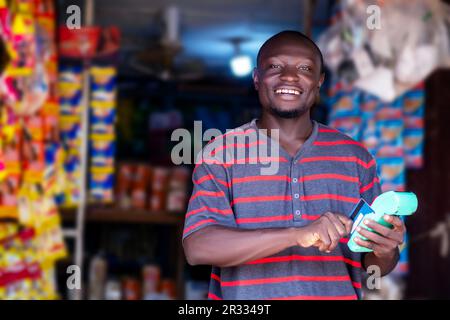 Foto eines jungen schwarzen afrikaners, der vor einem Laden einen Posterautomaten hält Stockfoto