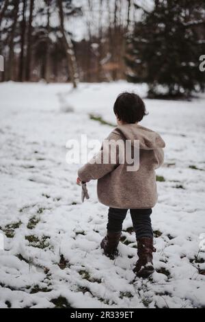 Ein kleiner Junge, der in einem verschneiten, kalten Winter draußen rennt Stockfoto