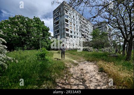 STEPNOHIRSK, UKRAINE - 19. MAI 2023 - Ein Mann mäht den Rasen außerhalb von Wohngebäuden, die durch mehrfache Beschießungen durch russische Truppen beschädigt wurden Stockfoto