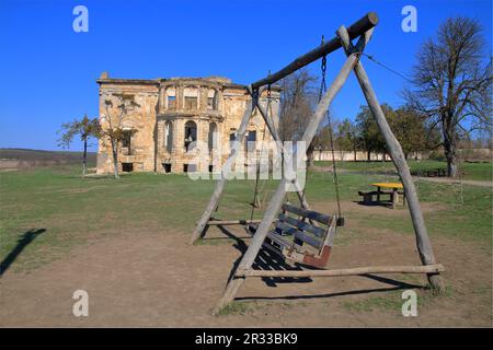 Das Foto zeigt eine hölzerne Schaukel vor dem Hintergrund der Ruinen des alten Palastguts der Dubetsky-Pankeyevs, die Wolfsschanze in der OD genannt wird Stockfoto