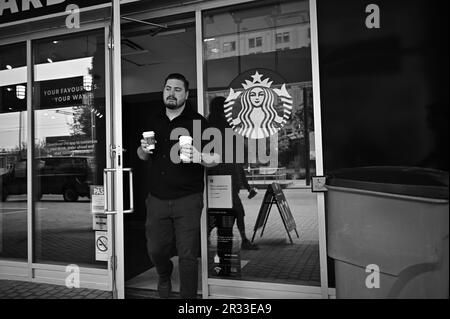 Schwarz-Weiß: Ein Mann verlässt das Starbucks Café mit zwei Tassen Kaffee in Toronto, Kanada Stockfoto