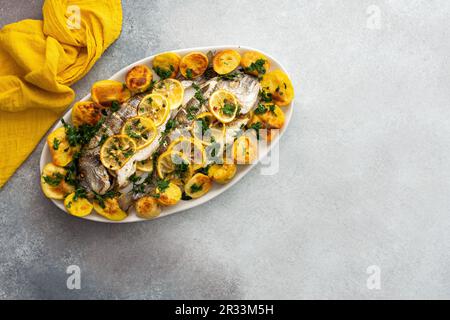 Im Ofen gebackener Dorada-Fisch mit Kartoffeln und Zitronenscheiben, gestreut mit Zitronensaft und pürierter Petersilie, gekochter Fisch in einem ovalen Gericht, Draufsicht Stockfoto