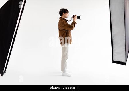 Vollbildaufnahme eines jungen Fotografen mit professioneller Fotokamera auf weißem Hintergrund Stockfoto