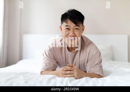 Porträt eines glücklichen, gutaussehenden chinesen, der auf dem Bett liegt Stockfoto