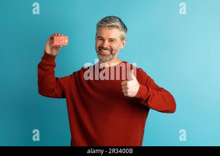 Fröhlicher, reifer Mann, der Bankkarte und Daumen hoch zeigt Stockfoto