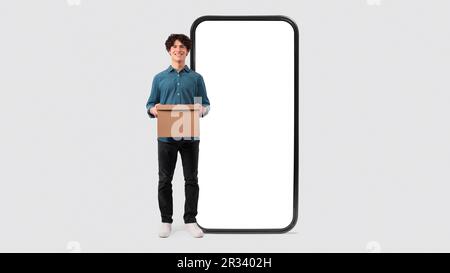 Mann Mit Karton In Der Nähe Eines Riesigen Telefons Auf Weißem Hintergrund Stockfoto