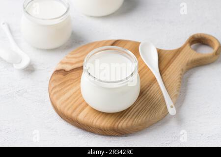 Natürlicher hausgemachter Joghurt in einem Glasgefäß auf einem Holzbrett auf hellgrauem Hintergrund Stockfoto