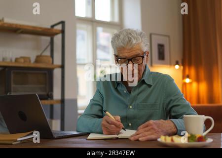 Ein älterer Mann, der Notizen in sein Tagebuch schreibt. Stockfoto