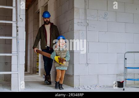 Vater und sein kleiner Sohn arbeiten in ihrem unvollendeten Haus, tragen hölzerne Panicle. Stockfoto