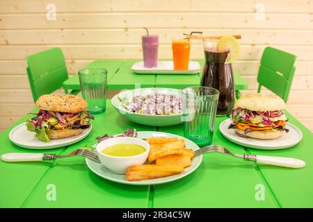 Ein heller grüner Restauranttisch mit peruanischen Gerichten mit Kassava, Gemüseburgern und Chicha Morada Saft Stockfoto