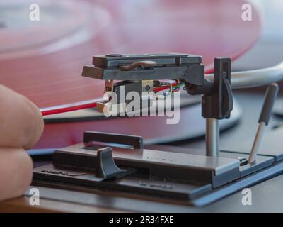 Detail einer männlichen Hand, die die Nadel auf die Spur einer roten Vinylplatte legt. Klassischer Plattenspieler Stockfoto